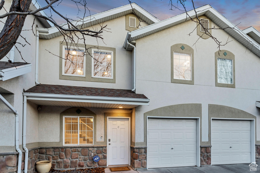 View of property featuring stucco siding, stone siding, an attached garage, driveway, and roof with shingles