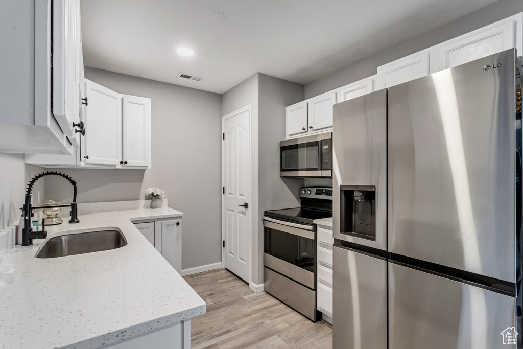Kitchen with appliances with stainless steel finishes, white cabinets, light wood-type flooring, and light stone counters
