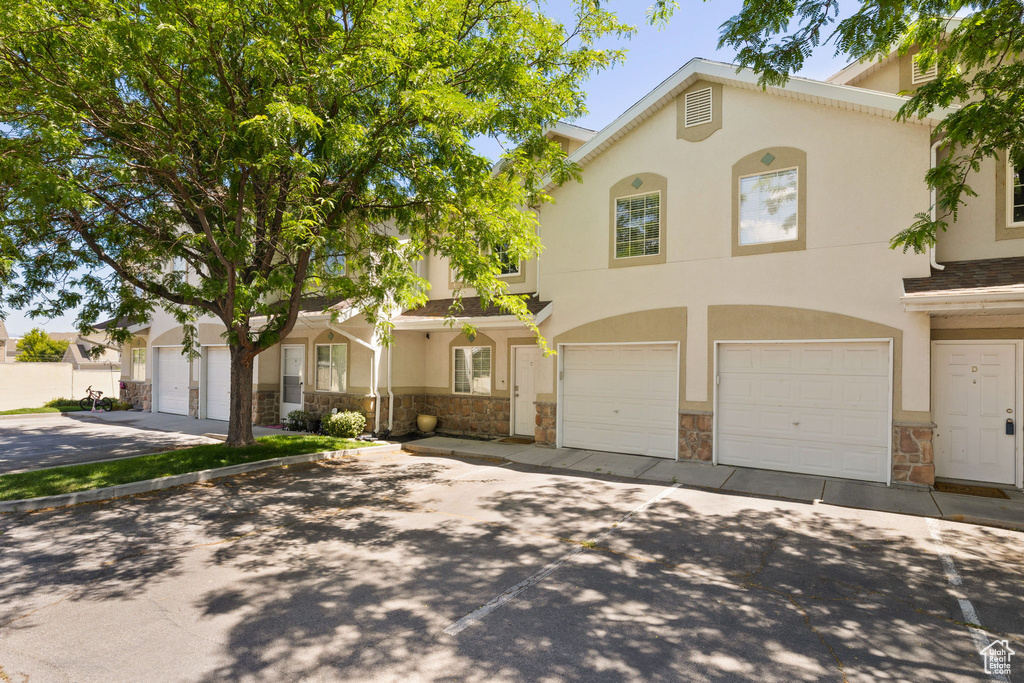 View of property with stone siding, a garage, stucco siding, and concrete driveway