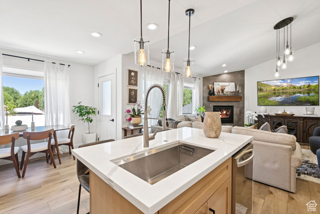 Kitchen featuring open floor plan, a tiled fireplace, light wood finished floors, stainless steel dishwasher, and recessed lighting