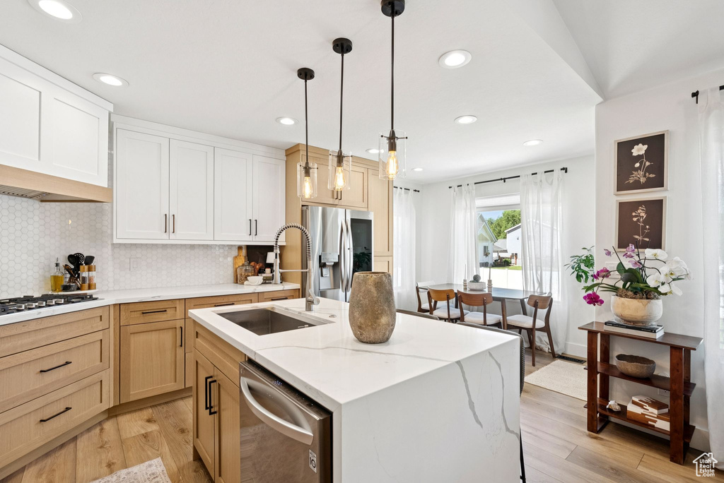 Kitchen featuring stainless steel appliances, light wood-style floors, decorative backsplash, a kitchen island with sink, and recessed lighting