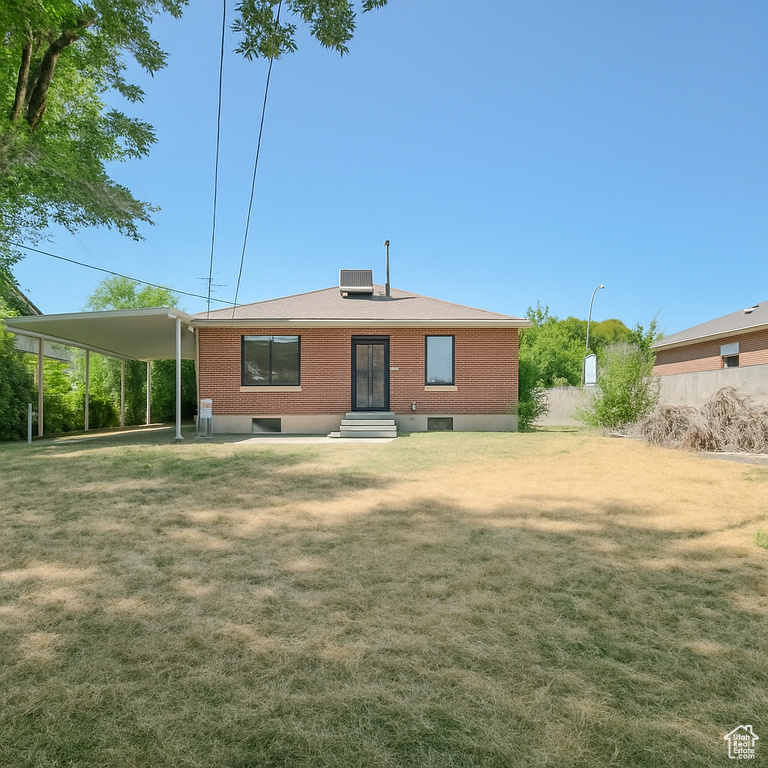 Back of property with a yard, brick siding, and an attached carport