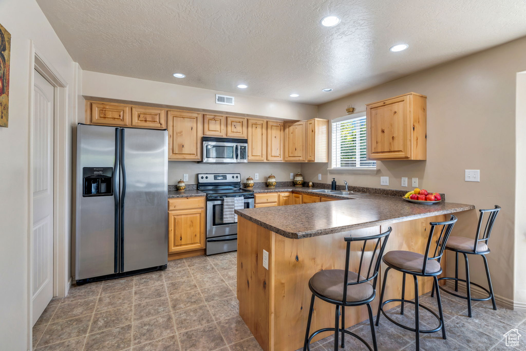 Kitchen featuring appliances with stainless steel finishes, a peninsula, dark countertops, a textured ceiling, and a breakfast bar area