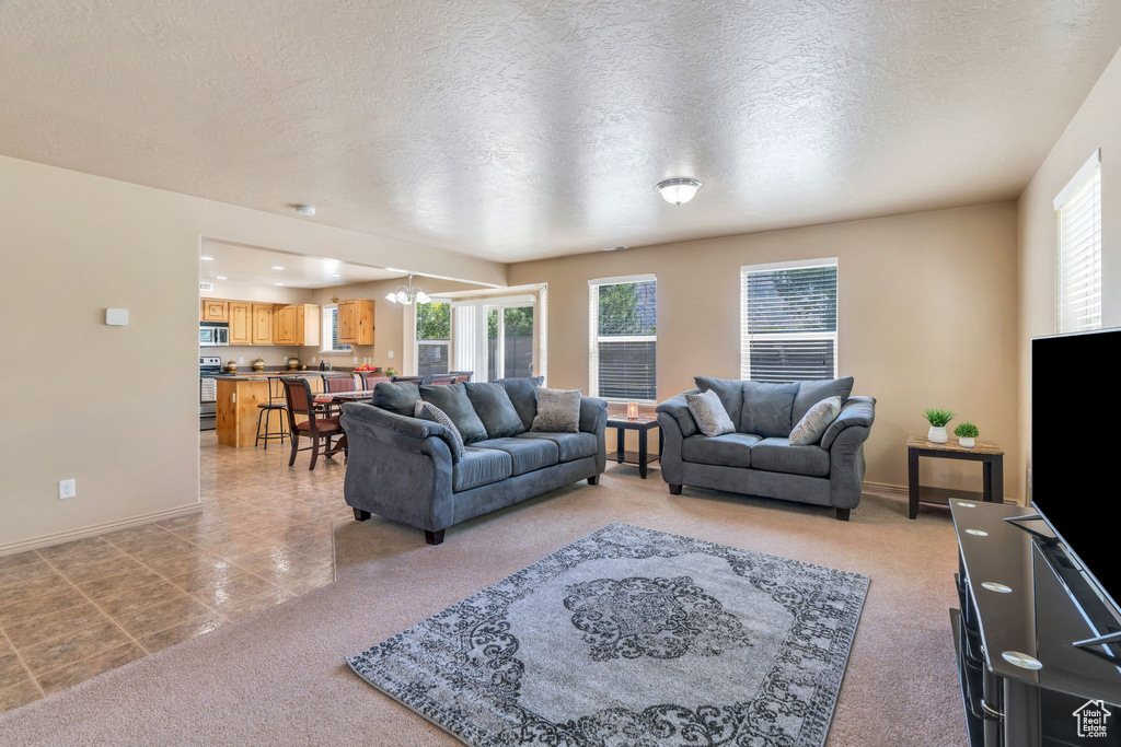 Living area with light colored carpet, a chandelier, a textured ceiling, and light tile patterned flooring