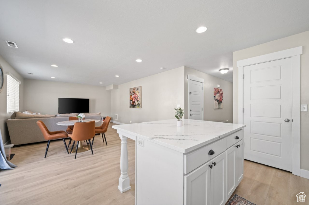 Kitchen featuring open floor plan, a kitchen island, light wood-type flooring, recessed lighting, and white cabinetry