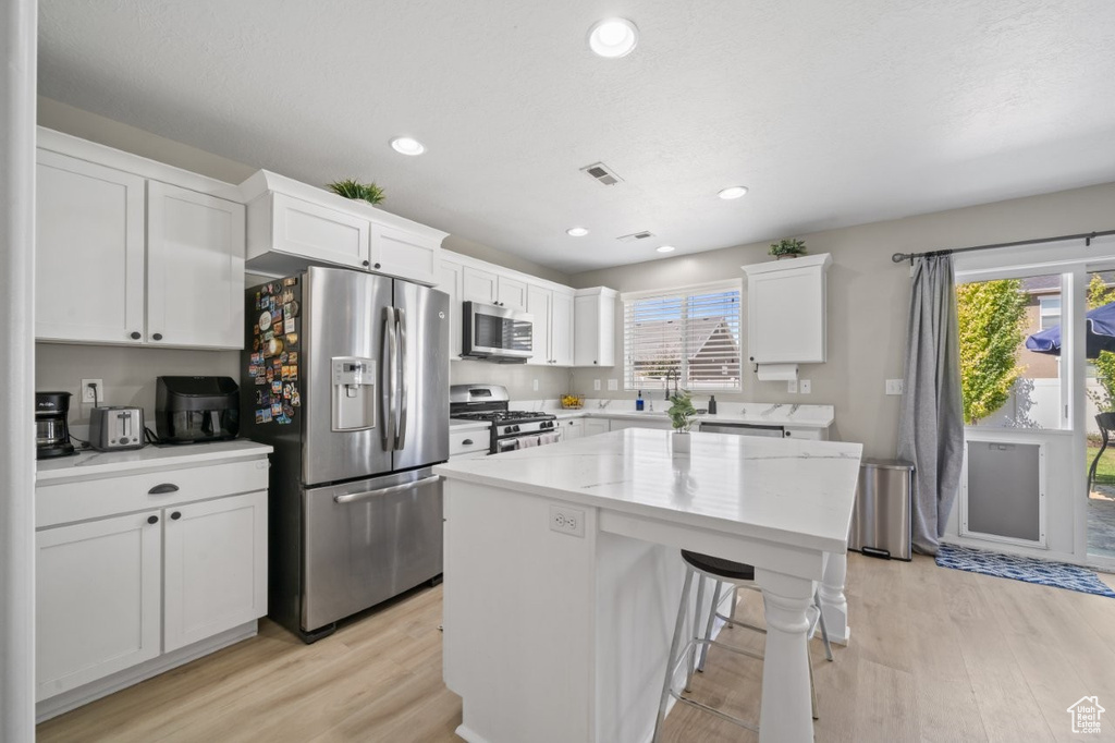 Kitchen featuring appliances with stainless steel finishes, light wood-type flooring, white cabinets, a center island, and plenty of natural light