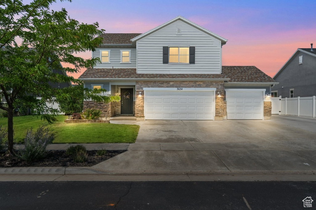 View of front of property with driveway, roof with shingles, stone siding, an attached garage, and a garage