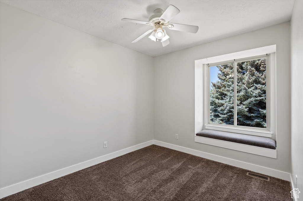 Empty room featuring dark colored carpet and ceiling fan