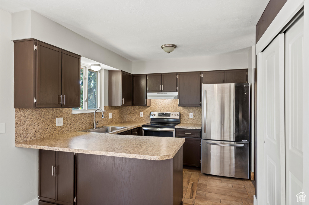 Kitchen with appliances with stainless steel finishes, under cabinet range hood, dark brown cabinets, light countertops, and a peninsula