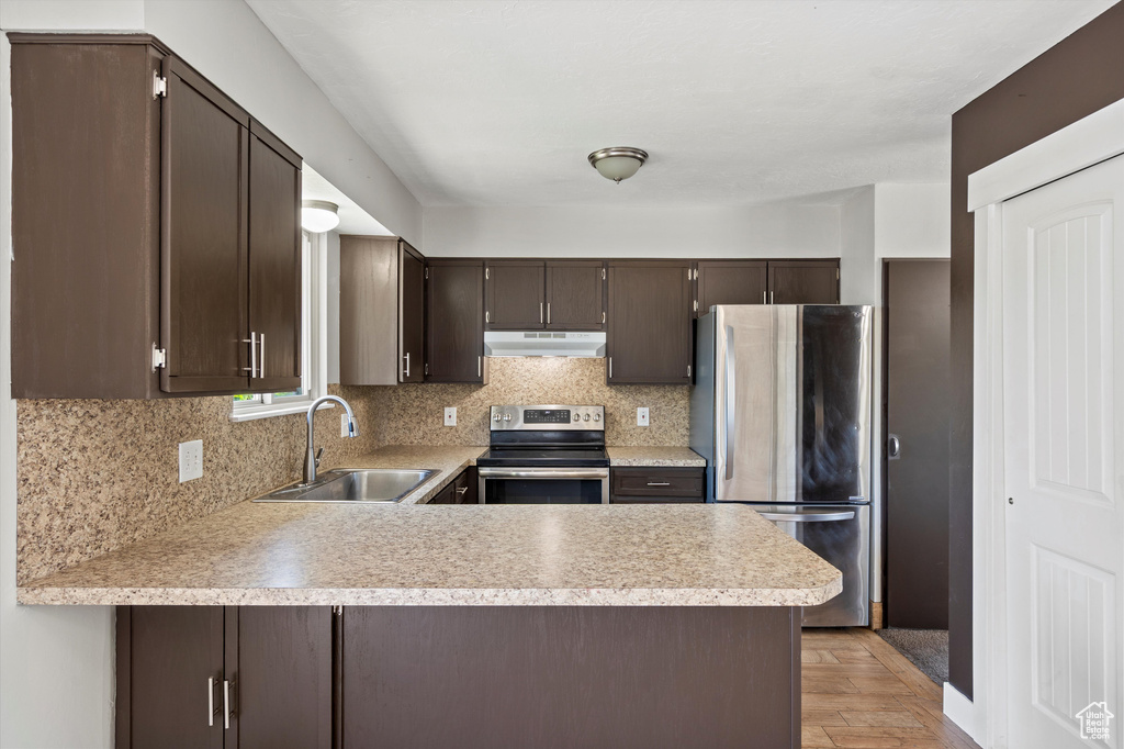 Kitchen with stainless steel appliances, under cabinet range hood, light countertops, dark brown cabinetry, and a peninsula