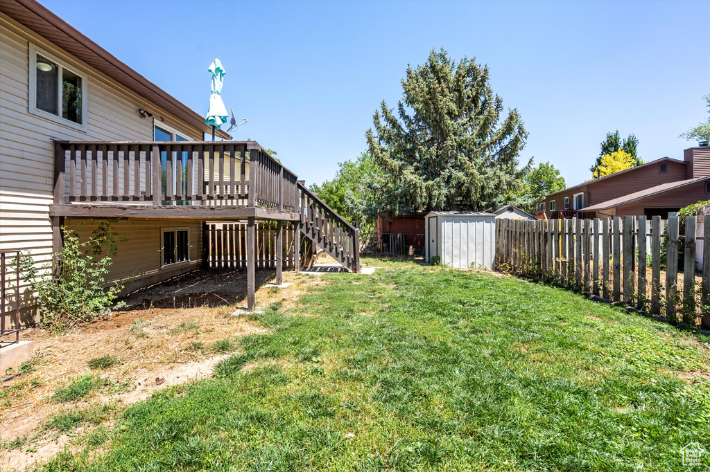 Fenced backyard featuring a storage unit, stairs, and a wooden deck