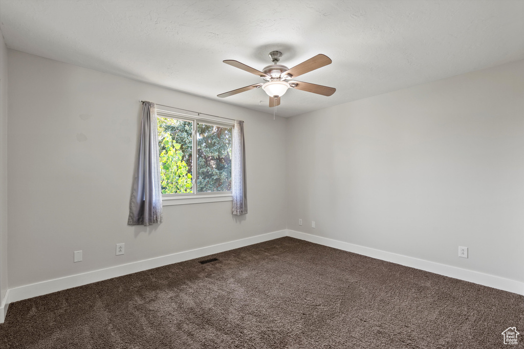 Unfurnished room with dark carpet and a ceiling fan