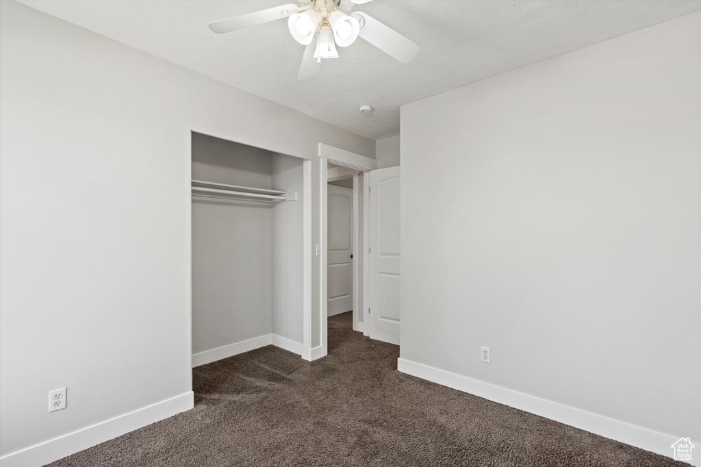 Unfurnished bedroom with dark carpet, a closet, and ceiling fan