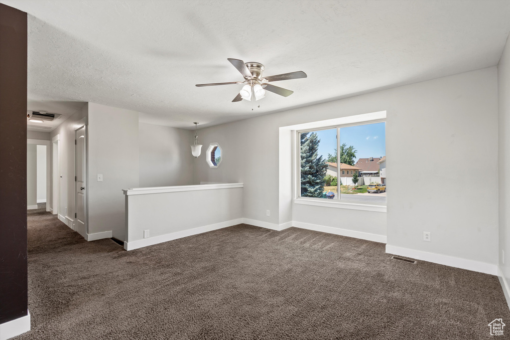 Empty room featuring ceiling fan and dark carpet