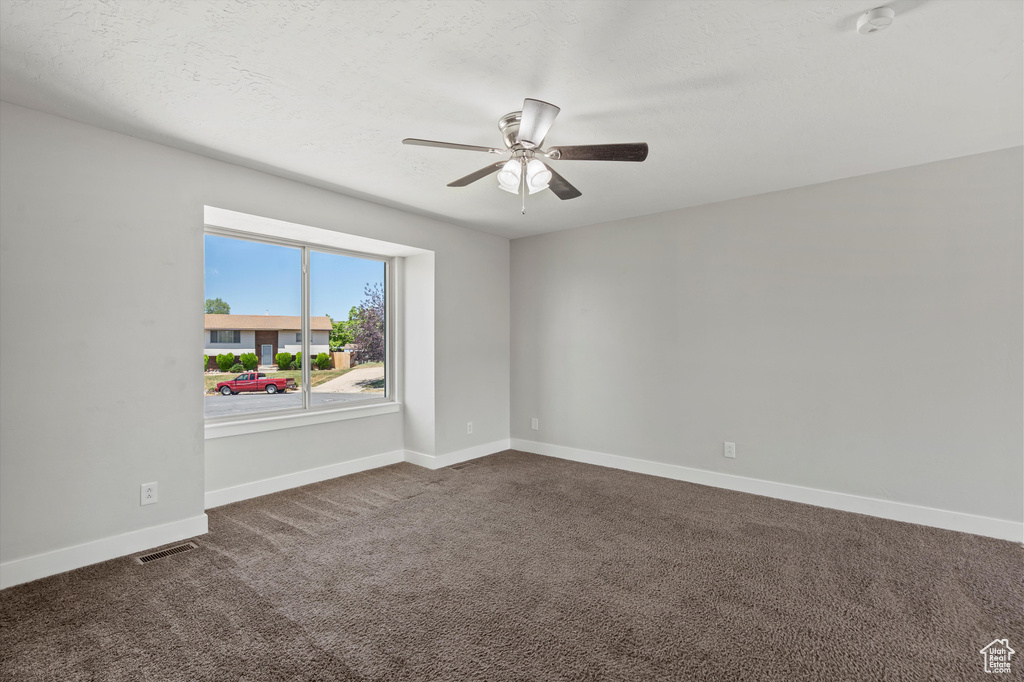 Spare room featuring a smoke detector, a ceiling fan, and dark colored carpet