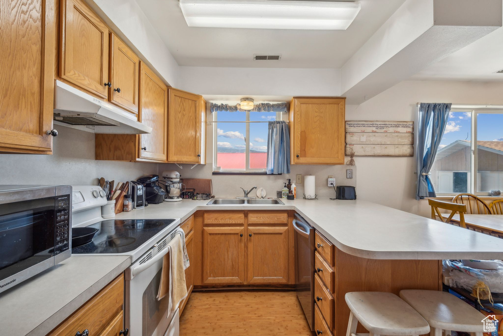 Kitchen featuring stainless steel appliances, a peninsula, under cabinet range hood, a breakfast bar, and light countertops