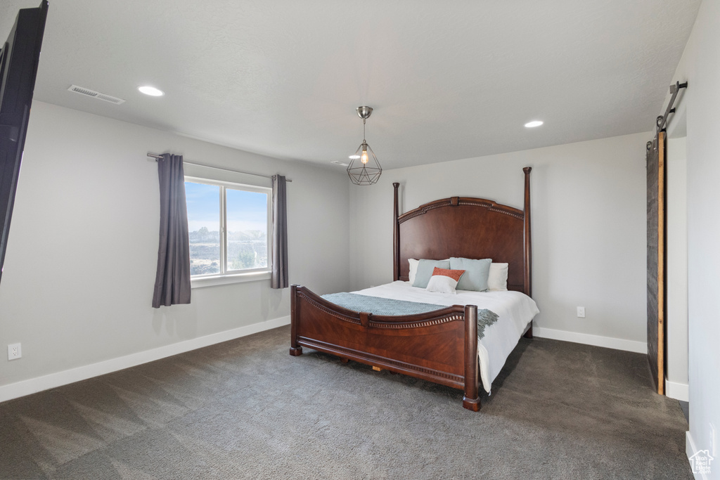 Bedroom with a barn door, recessed lighting, and dark colored carpet