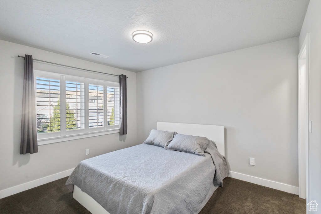 Bedroom with dark colored carpet and a textured ceiling