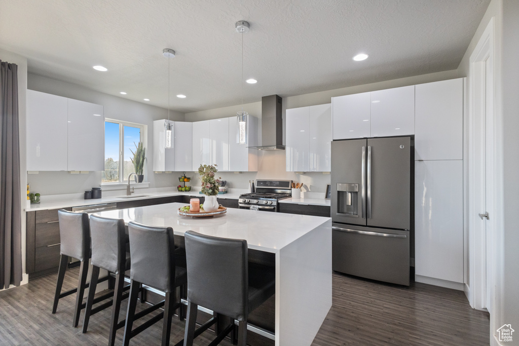 Kitchen with appliances with stainless steel finishes, wall chimney range hood, a kitchen breakfast bar, dark wood-style floors, and recessed lighting