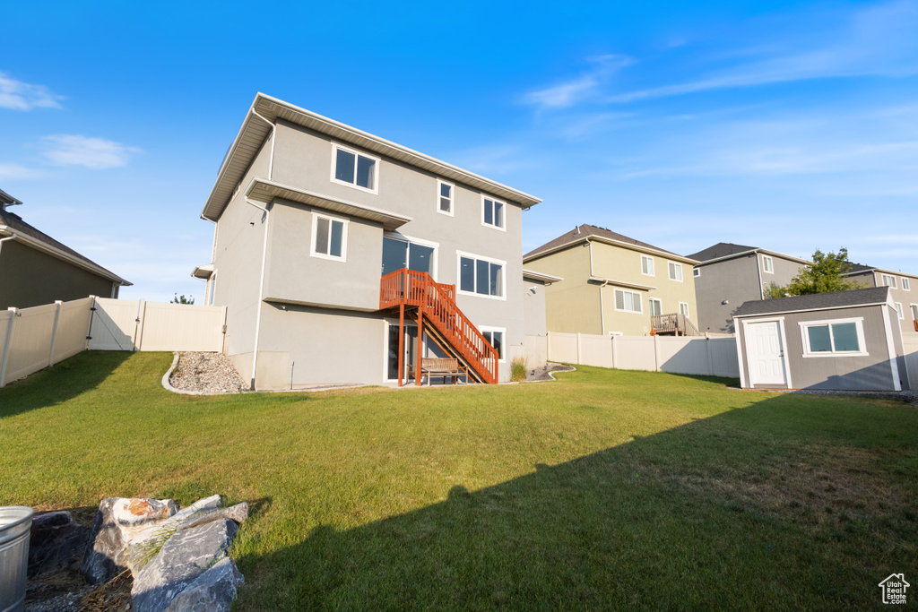 Rear view of house with a fenced backyard, a storage unit, stairs, stucco siding, and a residential view