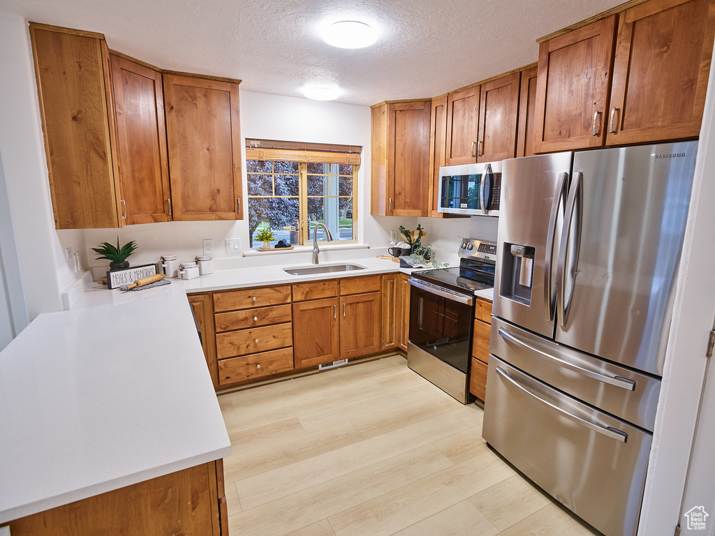 Kitchen featuring stainless steel appliances, brown cabinets, a textured ceiling, light wood finished floors, and light countertops
