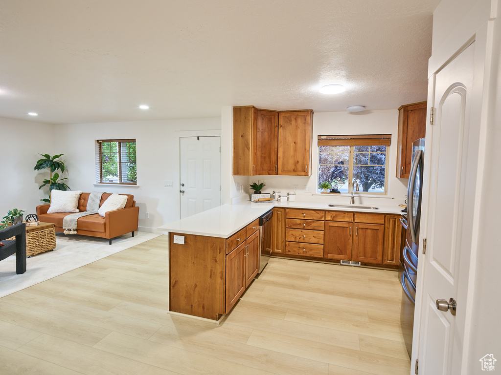 Kitchen with a peninsula, stainless steel dishwasher, brown cabinets, light countertops, and open floor plan