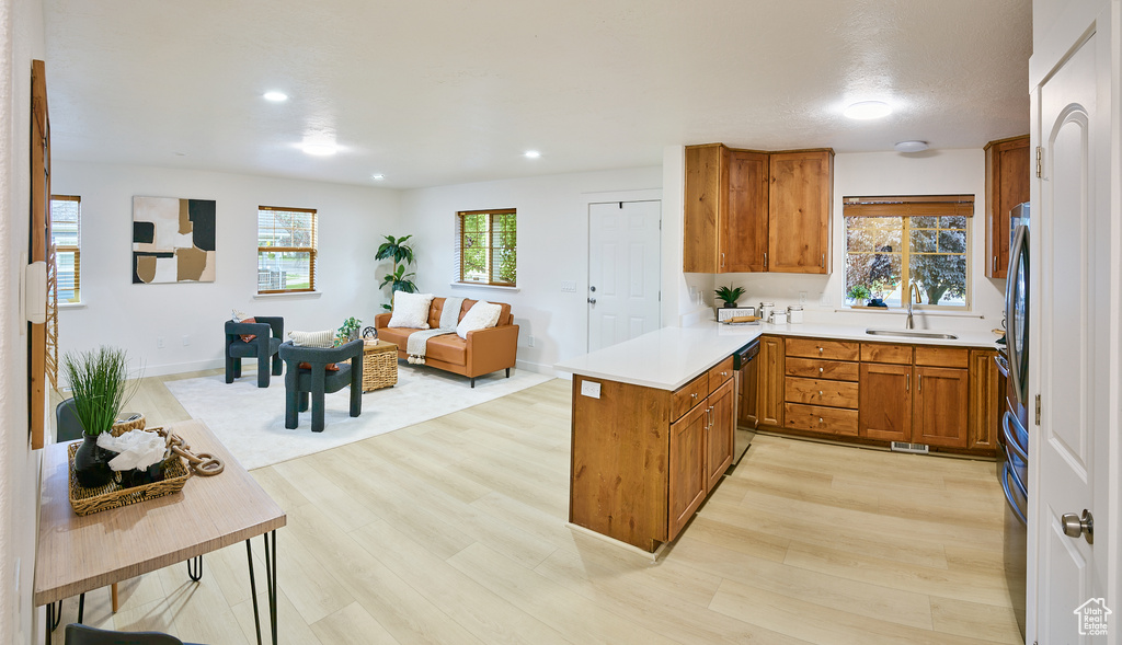 Kitchen with brown cabinetry, dishwasher, light wood finished floors, a peninsula, and open floor plan