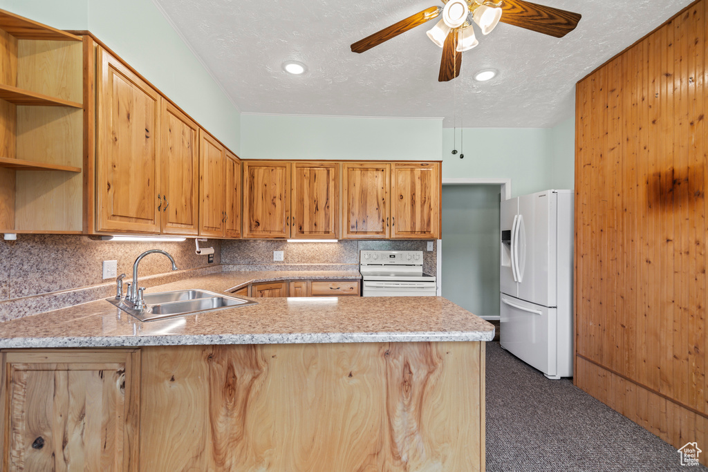 Kitchen with white appliances, a peninsula, dark carpet, tasteful backsplash, and ceiling fan