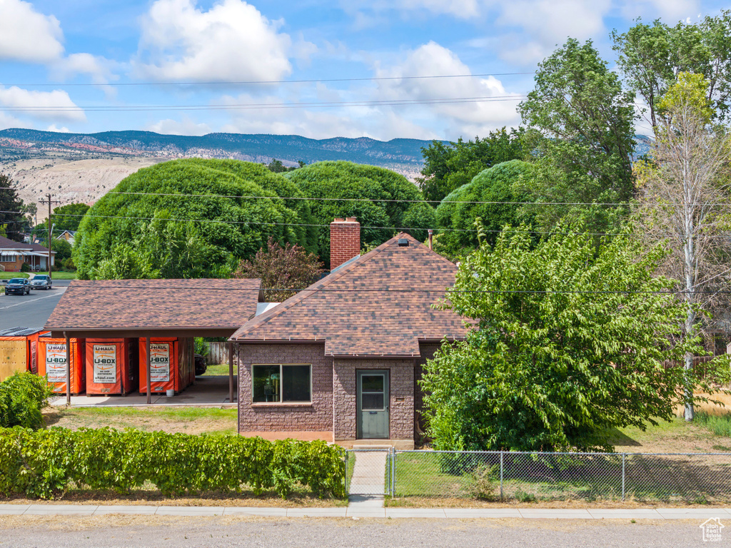 View of front facade with a fenced front yard, roof with shingles, a mountain view, a chimney, and brick siding