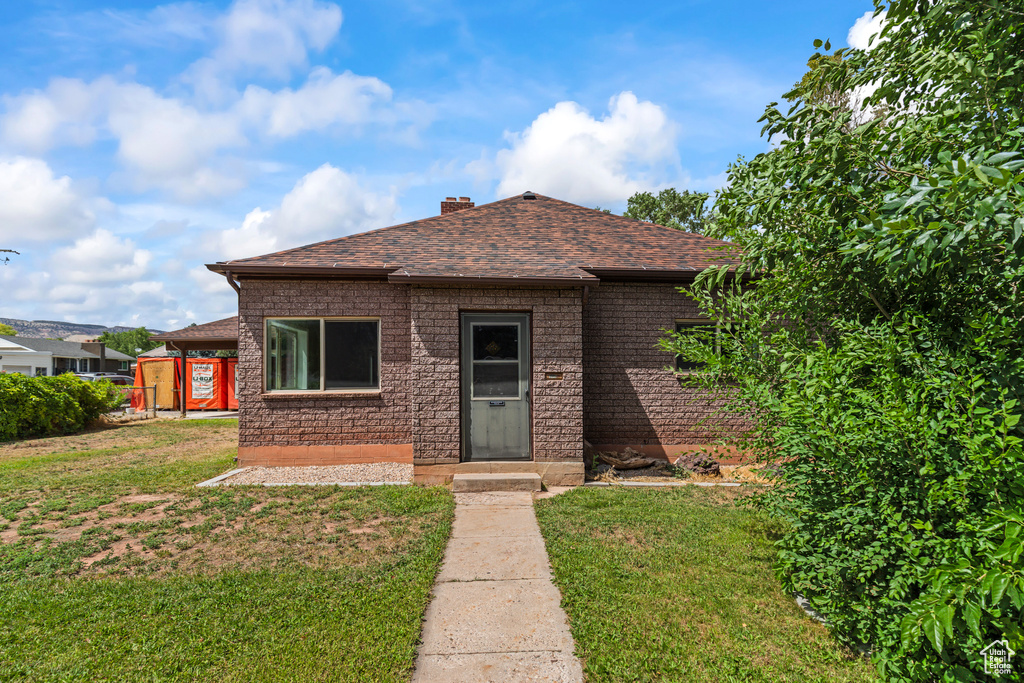 View of front facade with a front yard, a chimney, and a shingled roof