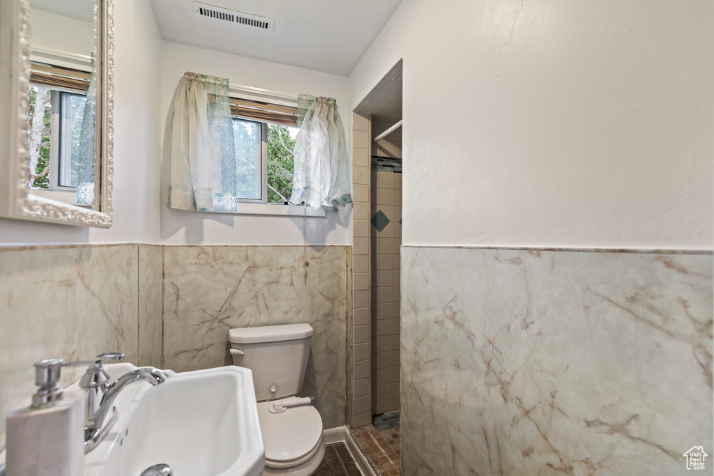 Full bathroom with tile walls, tiled shower, and wainscoting