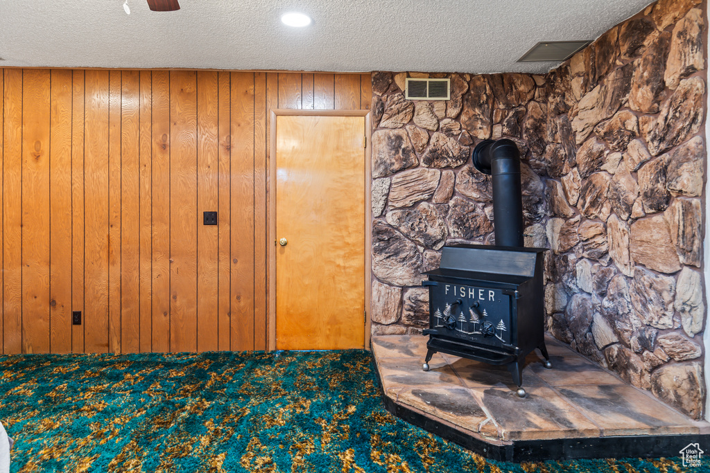 Detailed view of a textured ceiling, a wood stove, wooden walls, and carpet