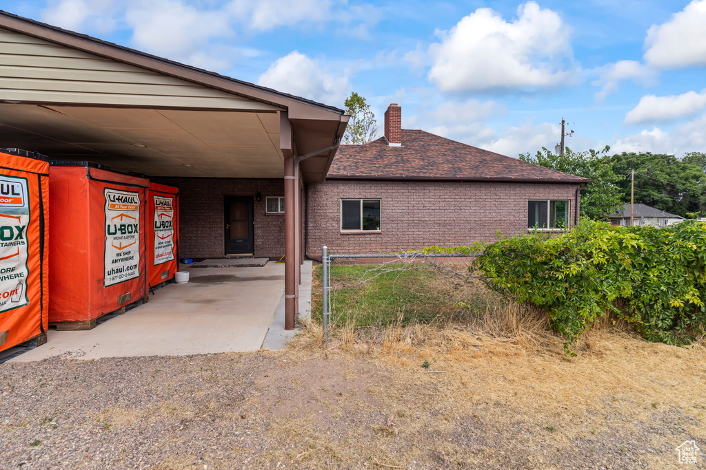 View of side of home with a chimney, a carport, roof with shingles, and brick siding