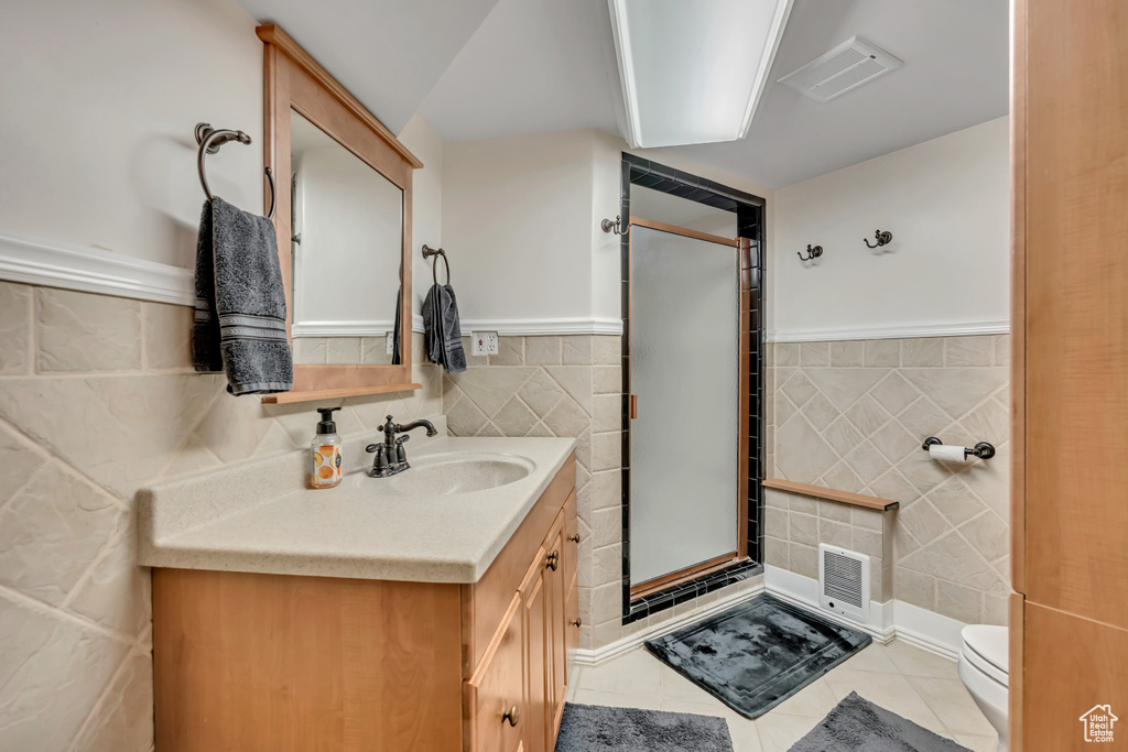 Bathroom with tile walls, vanity, a shower stall, tile patterned floors, and wainscoting