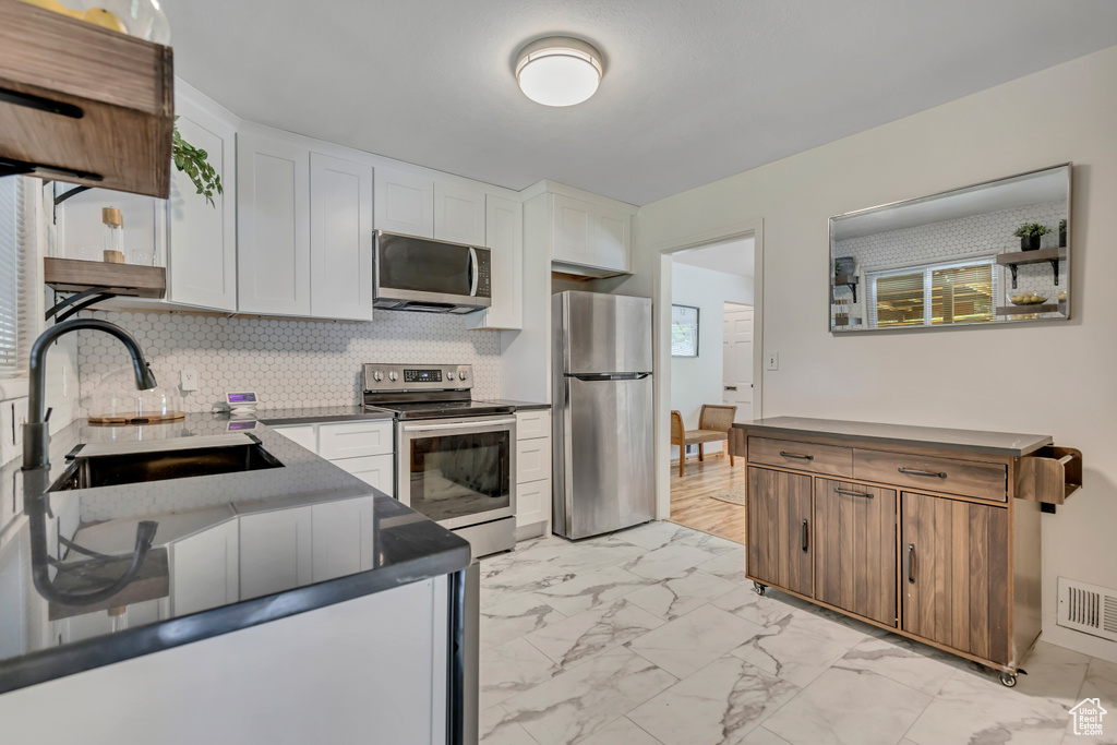 Kitchen with stainless steel appliances, light marble finish flooring, white cabinets, backsplash, and dark countertops