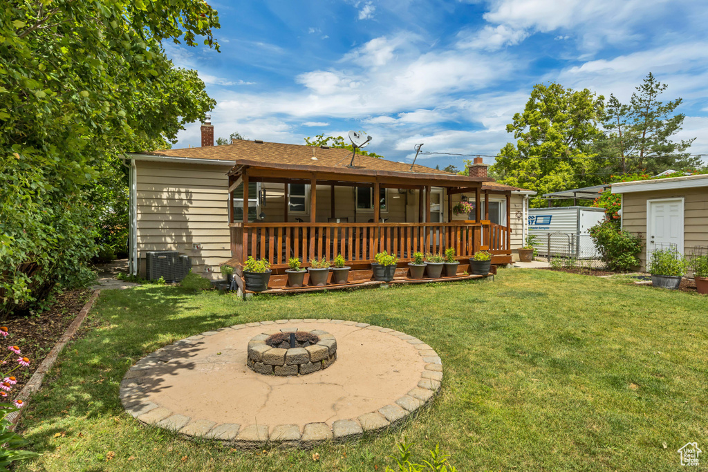 Back of property with a chimney, a lawn, an outdoor fire pit, and a deck