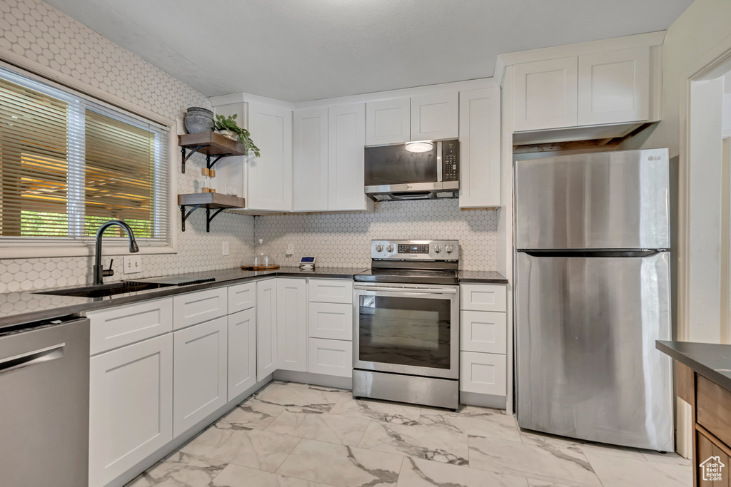 Kitchen featuring appliances with stainless steel finishes, light marble finish floors, white cabinetry, open shelves, and backsplash