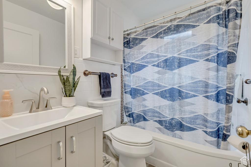Bathroom featuring vanity, tile walls, shower / bath combo with shower curtain, and tasteful backsplash