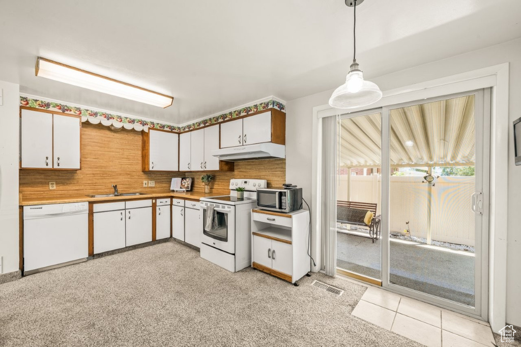 Kitchen with white appliances, under cabinet range hood, hanging light fixtures, and tasteful backsplash
