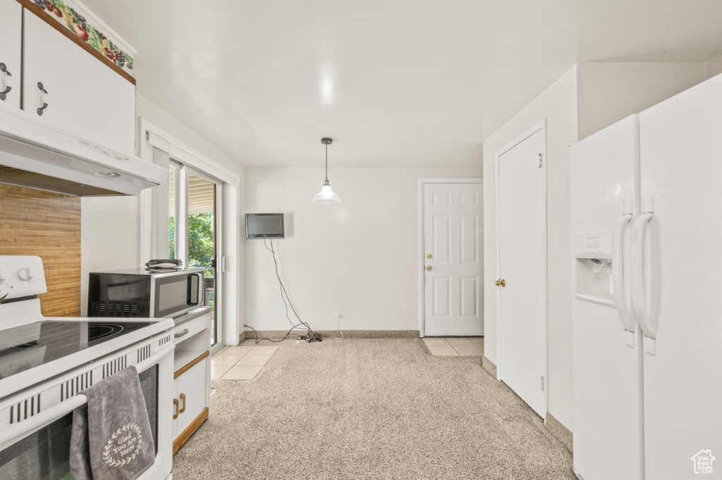 Kitchen with white appliances, exhaust hood, white cabinets, and light colored carpet