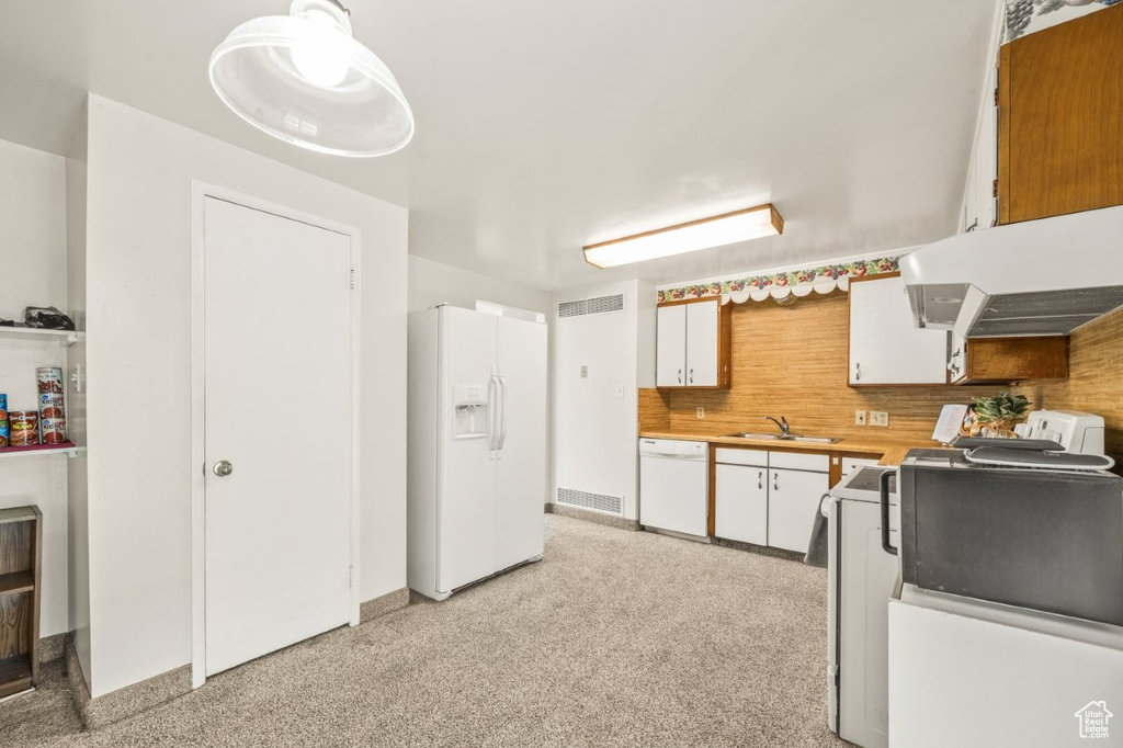 Kitchen featuring white appliances, light countertops, white cabinets, decorative backsplash, and under cabinet range hood