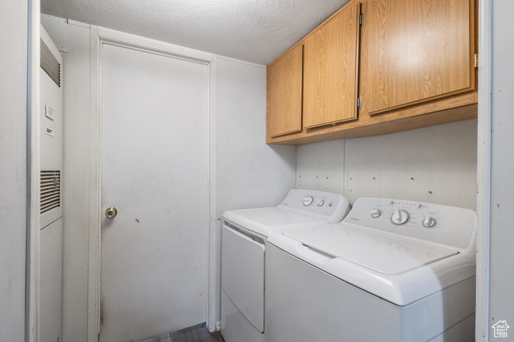 Laundry room with cabinet space, washing machine and clothes dryer, and a textured ceiling