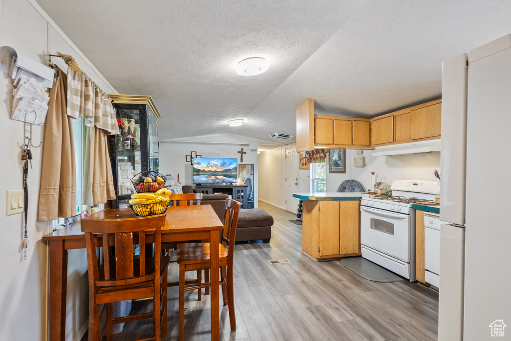 Kitchen with white appliances, a peninsula, under cabinet range hood, vaulted ceiling, and light wood finished floors