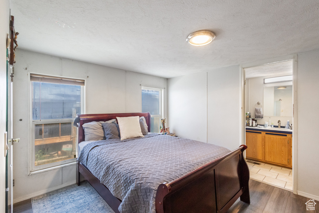 Bedroom with ensuite bath, light wood-style floors, and a textured ceiling