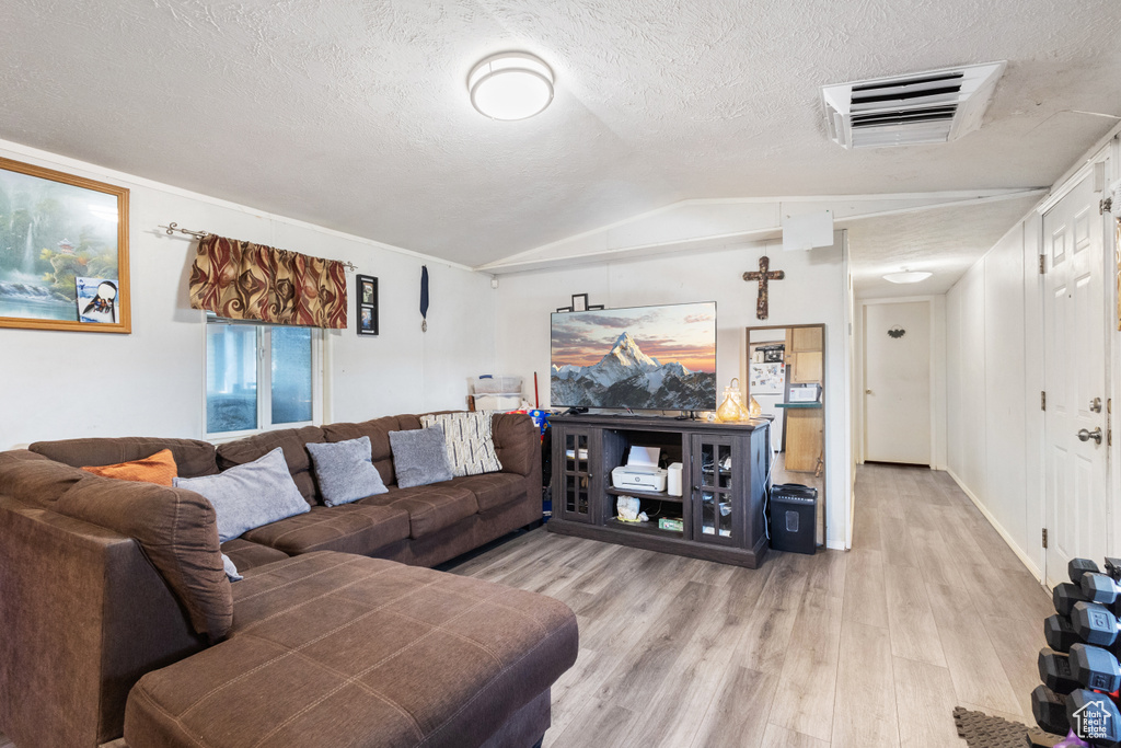 Living room featuring light wood-style flooring, vaulted ceiling, and a textured ceiling
