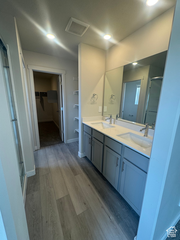 Bathroom with a stall shower, a spacious closet, double vanity, wood finished floors, and recessed lighting