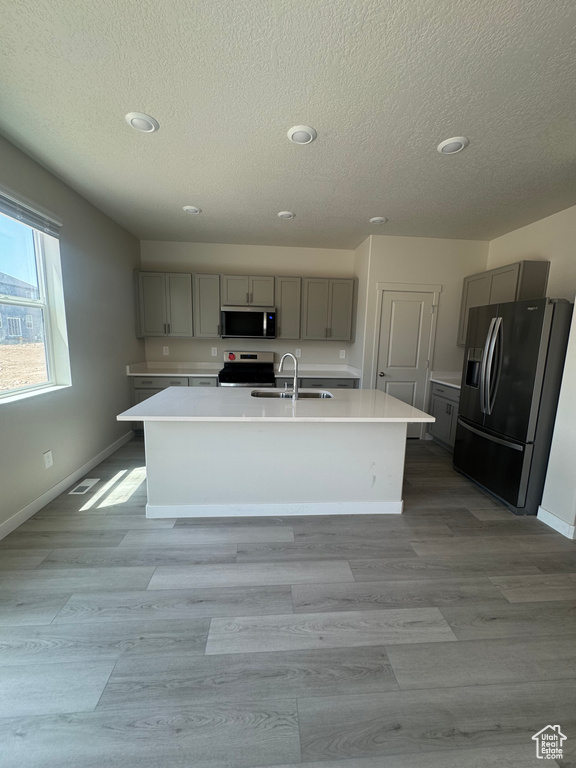 Kitchen featuring gray cabinetry, stainless steel appliances, a textured ceiling, recessed lighting, and a center island with sink