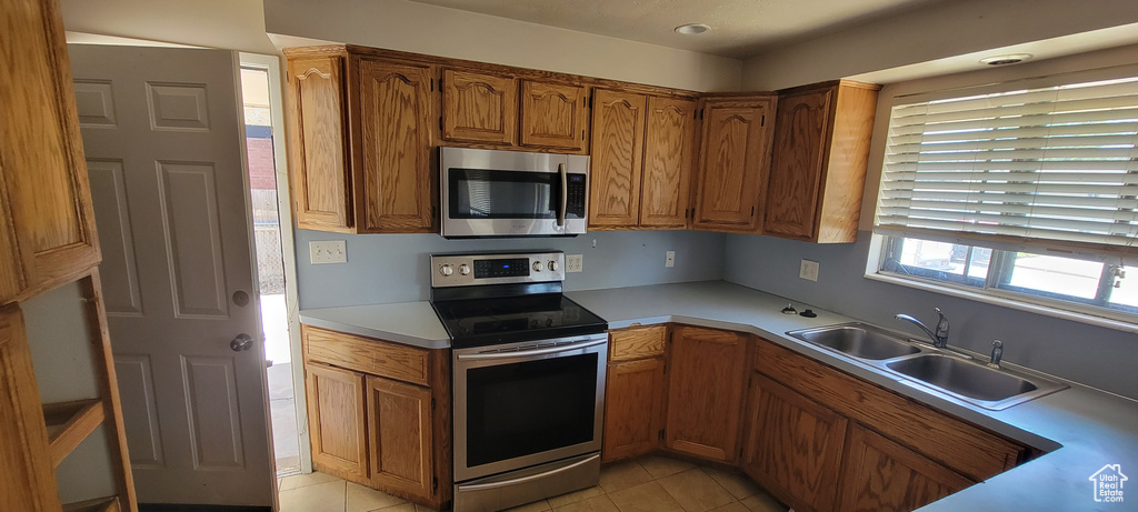 Kitchen with appliances with stainless steel finishes, brown cabinets, light tile patterned flooring, light countertops, and recessed lighting