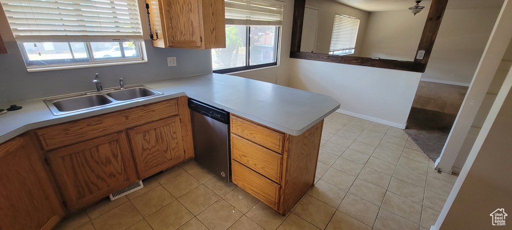 Kitchen featuring stainless steel dishwasher, a peninsula, light countertops, brown cabinets, and light tile patterned floors