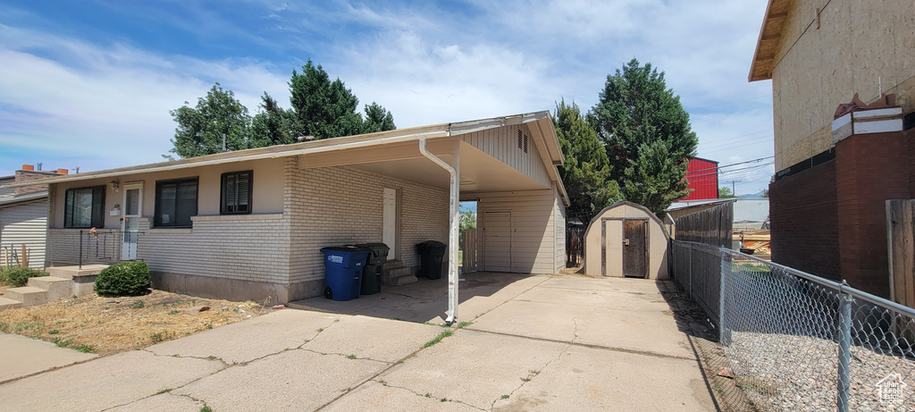 View of side of home featuring a storage shed, driveway, brick siding, and a carport